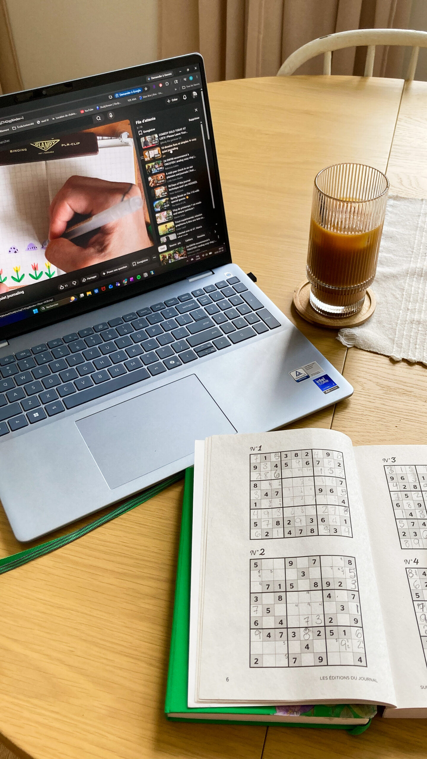 Sur une table il y a un ordinateur un café glacé et un sudoku